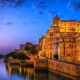 Panoramic view of Udaipur city with Lake Pichola, City Palace, and Aravalli hills during sunset.